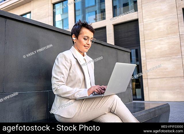 Businesswoman using laptop while sitting on bench in city