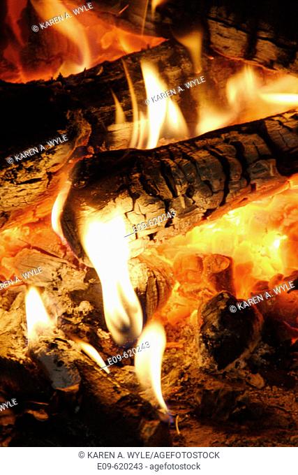 detail of fire in fireplace, glowing coals, yellow-white flames at ends of logs and in embers
