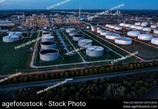 04 October 2022, Saxony-Anhalt, Leuna: Behind the illuminated tank farm, the facilities of the Total refinery and the chemical park rise into the air (aerial...