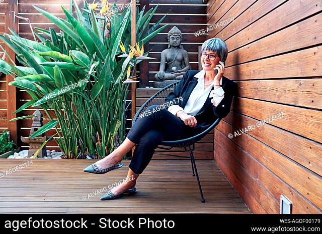Smiling businesswoman talking on smart phone while sitting at backyard