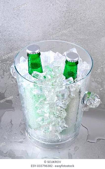 Two green beer bottles in a crystal ice bucket sitting on a wet stainless steel surface. Vertical Format with shallow depth of field