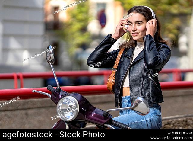 Smiling woman with headphones on motor scooter