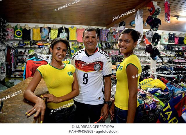 A man wears a jersey of the German national soccer team (C) and two girls wearing t-shirts of the Brazilian team pose for a photo in their shop in a village...