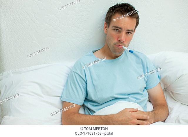 Sick man taking temperature with digital thermometer