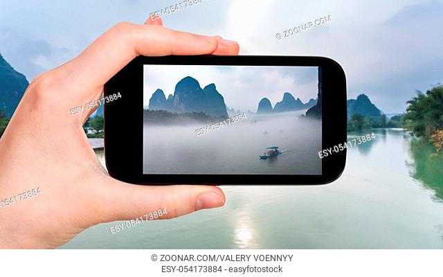 travel concept - tourist photographs ships in fog on river near Xingping town in Yangshuo county in spring morning in China on smartphone