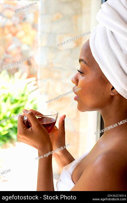 Happy african american wearing towel and holding cup of tea in bathroom
