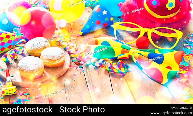 Colorful carnival or party background with donuts, balloons, streamers and confetti and funny face formed from wig, nose and glasses on rustic wooden planks...