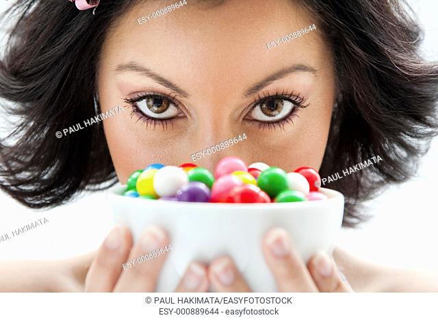 Beautiful candy girl closeup holding a bowl of colorful bubblegum candy balls in front of her face