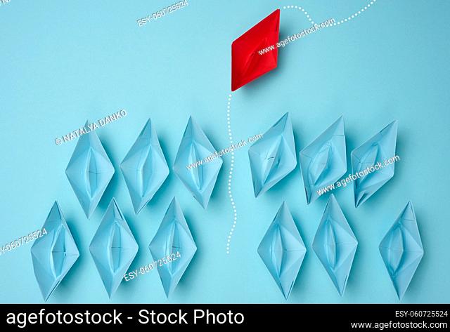 a group of blue paper boats heading in one direction and one red one heading in the opposite direction. The concept of individuality