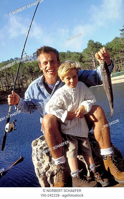 outdoor, portrait, blond 6-year-old boy and his father sit holding a fishing rod and a fish in their hands at the shore of a lake  - GERMANY, 19/09/2004