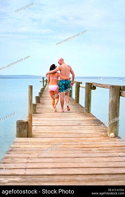Affectionate couple hugging and walking on wooden pier