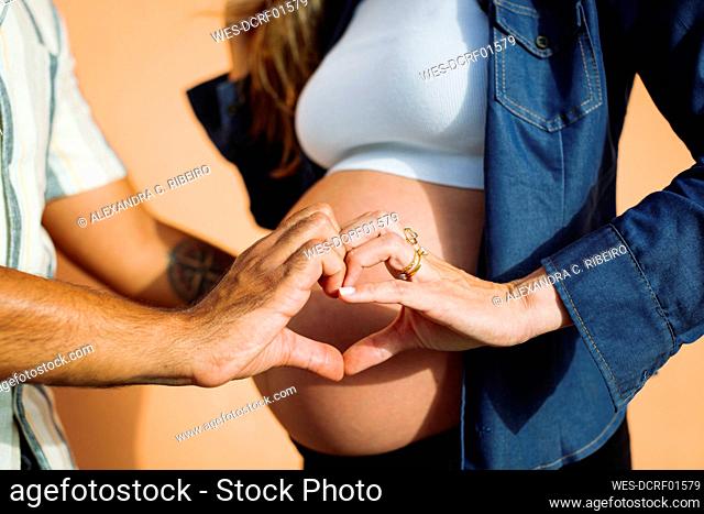 Man making heart shape with pregnant woman