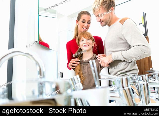 Portrait of a happy family with one child looking at camera, while posing together in the interior of a modern sanitary ware shop with various bathroom faucets...