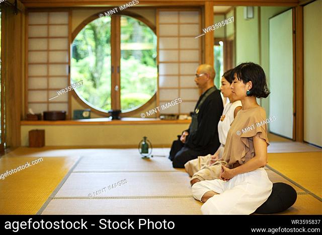 Two Japanese women and Buddhist priest kneeling in Buddhist temple, praying