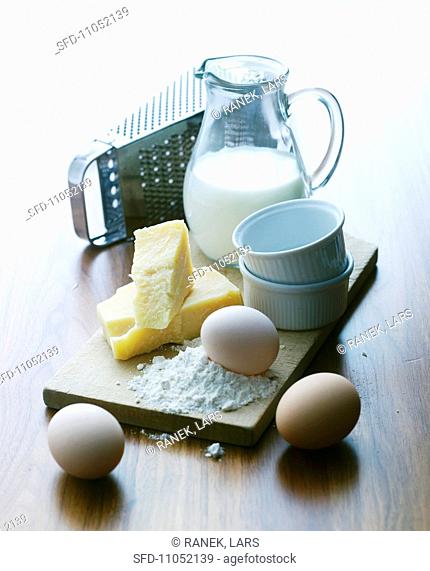 An arrangement of souffle ramekins, eggs, cheese, a cheese grater and milk