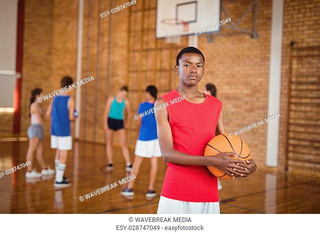 High school boy holding a basketball while team playing in background