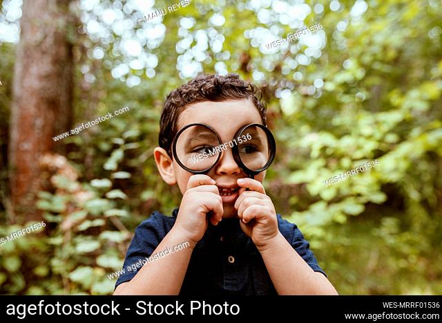 Cute boy looking through magnifying glass in forest