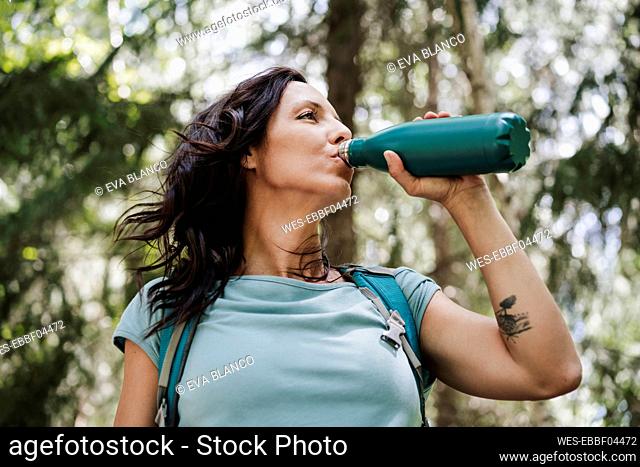 Mid adult woman drinking water from bottle in forest
