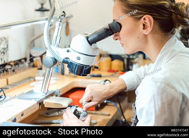 Diligent jeweler working on microscope at her workbench on some jewelry