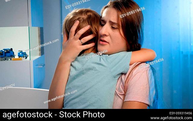 Portrait of young loving mother soothing and caressing scared little boy in children room at night. CHild being scared and crying of nightmare or bad dream
