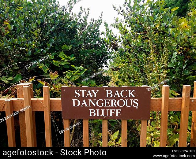 brown stay back dangerous bluff sign on wood fence with green plants