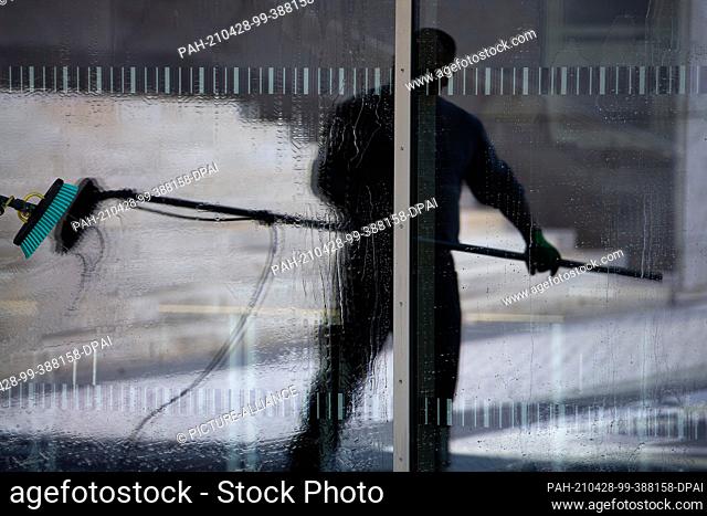 28 April 2021, Hessen, Fulda: A man is reflected in a window he is cleaning. Photo: Sebastian Gollnow/dpa. - Fulda/Hessen/Germany