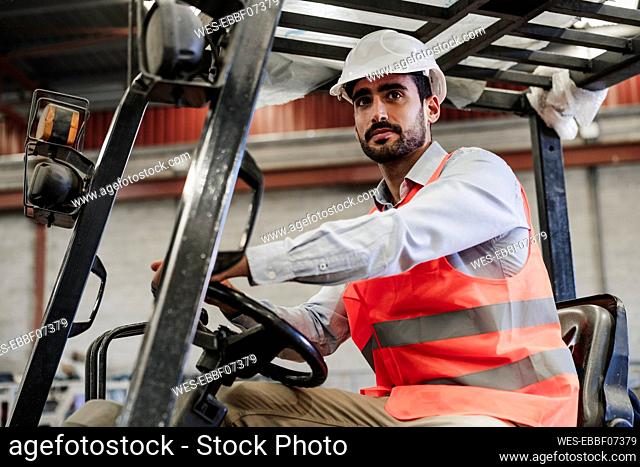 Engineer wearing protective workwear driving forklift in industry