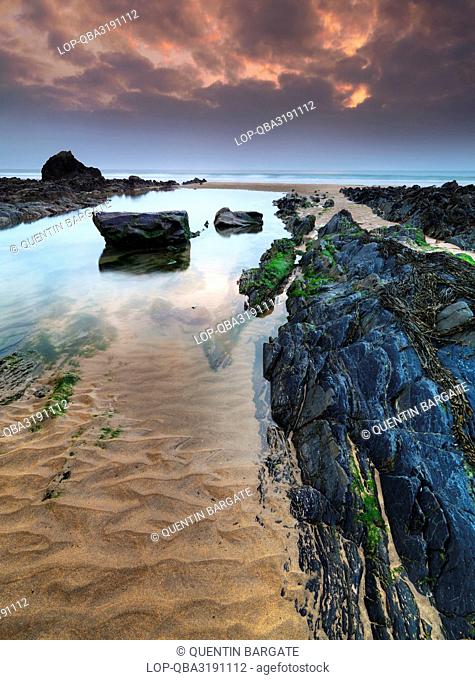 England, Cornwall, Sandy Mouth. Rock formations and pools of water on Sandy Mouth beach at dusk