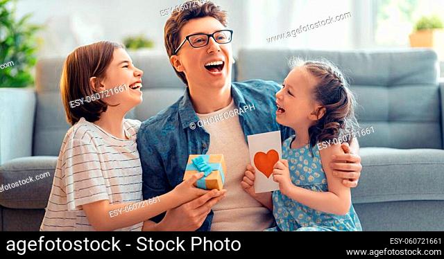 Children daughters are congratulating their father and giving him postcard. Dad and girls are smiling and hugging. Family holiday and togetherness