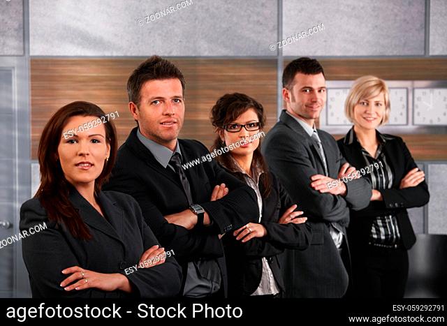 Portrait of business people standing in a row on office corridor, looking at camera