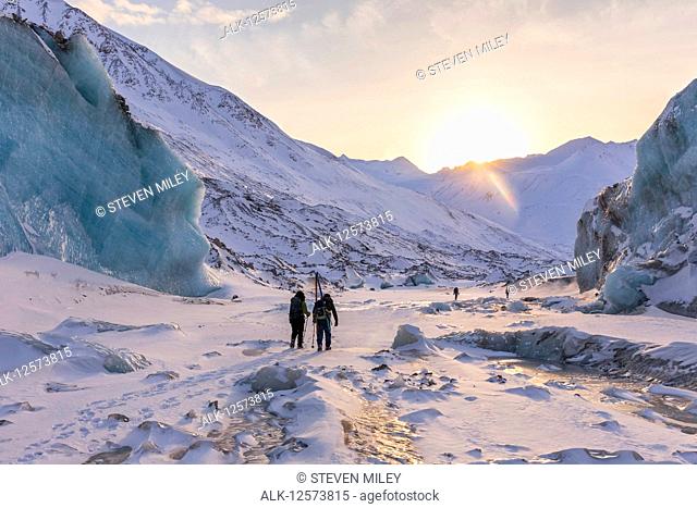 Winter hikers explore Black Rapids Glacier as the sun sets over the Alaska Range; Alaska, United States of America