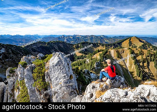 hiker on the blankenstein enjoys the view over the bavarian prealps on a sunny day in autumn. mountains, hills and forests under a blue sky