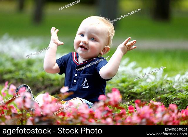 Cheerful kid on the grass claps his hands.Emotion of admiration. Joyous baby on the street