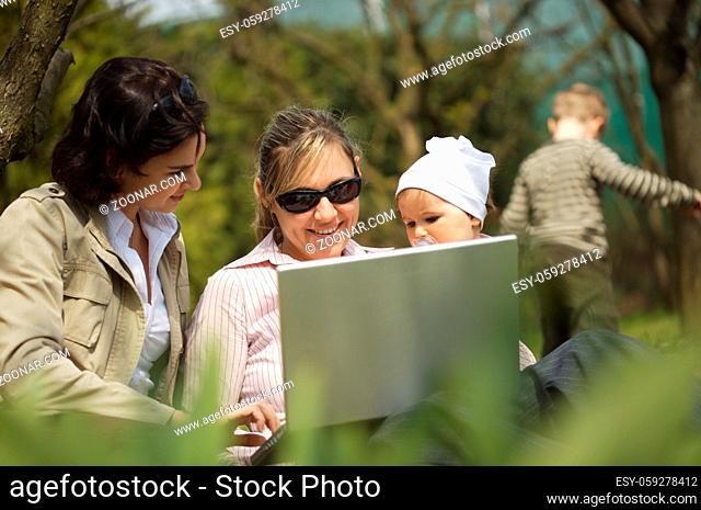 Young mothers are sitting on the ground in the garden and using a laptop