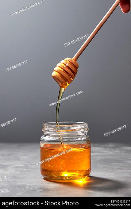 Fragrant natural organic noney dripping from wooden stick into a gray kitchen table, place under text, pure natural sweet goodness