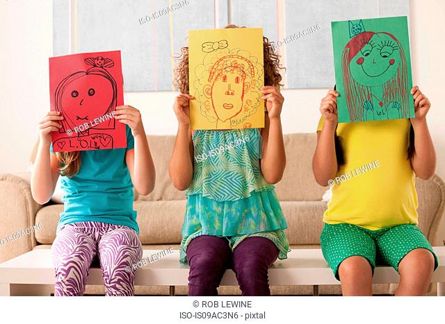 Three girls holding pictures over faces