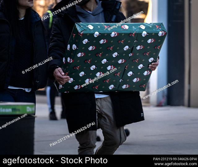 13 December 2023, Hesse, Frankfurt/Main: A passer-by carries a Christmas-wrapped parcel along Frankfurt's Zeil shopping street Photo: Frank Rumpenhorst/dpa