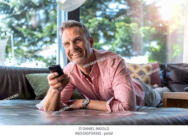 Smiling mature man lying on couch at home using remote control