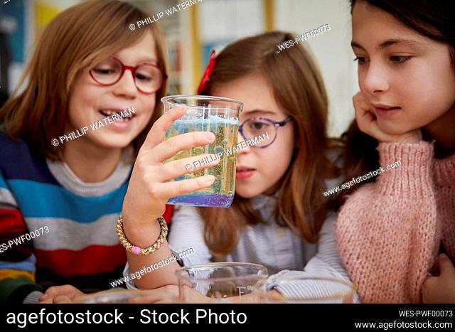 Three children looking at liquid in a science chemistry lesson