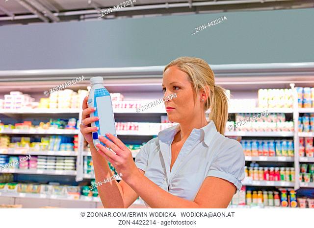 Eine junge Frau kauft Milch im Supermarkt. Steht vor dem Kühlregal
