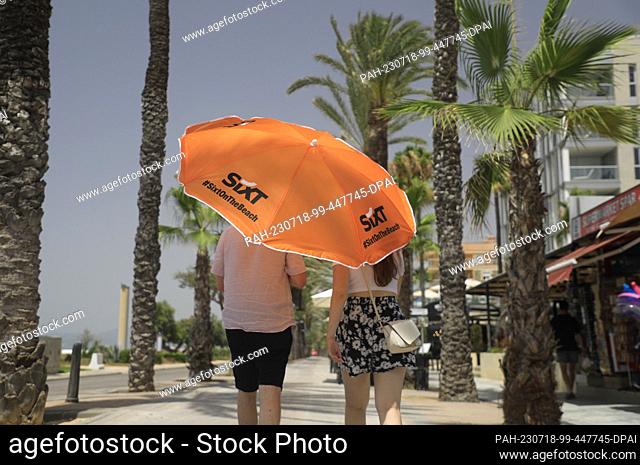 18 July 2023, Spain, Palma de Mallorca: People walk with an umbrella on the beach promenade of Arenal in hot temperatures