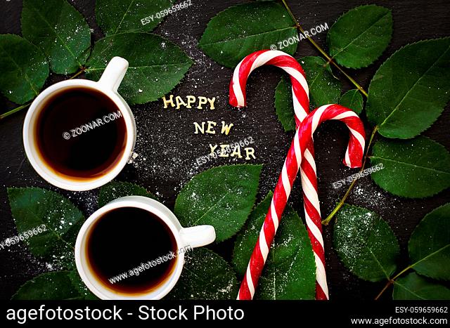 inscription of new year on a black board with sprigs of leaves and red candy
