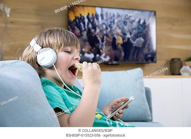 A child playing with a smartphone next to the television
