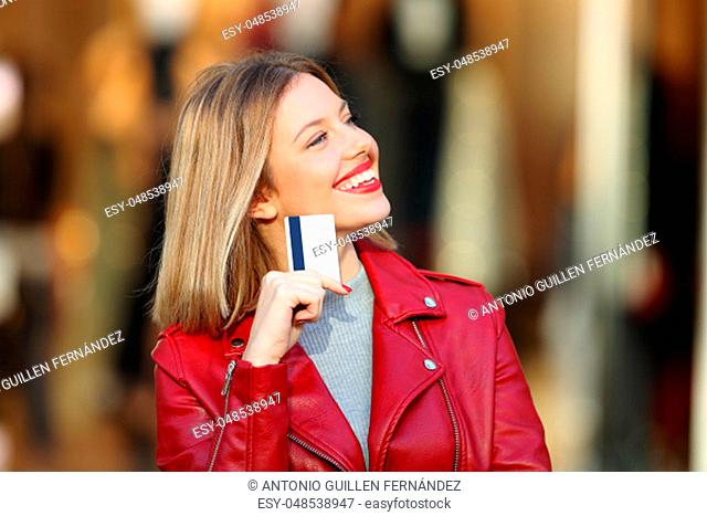 Portrait of a happy shopper wondering what to buy holding a credit card with a storefront in the background