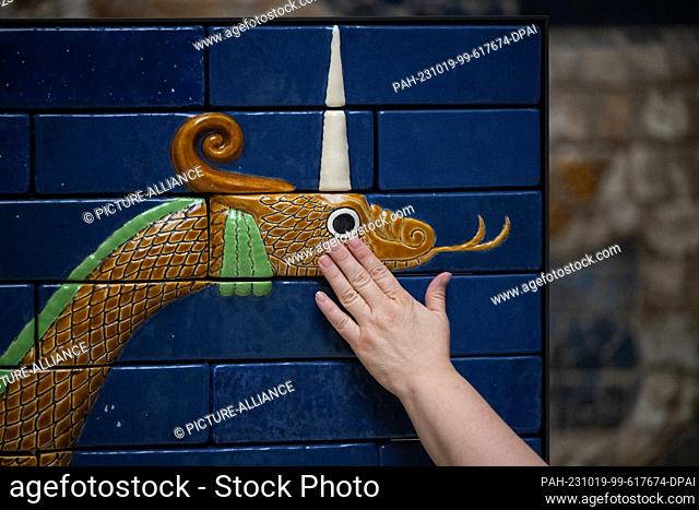 PRODUCTION - 17 October 2023, Berlin: A visitor strokes a replica of tiles on the Ishtar Gate of Babylon, built for this purpose, in the Pergamon Museum