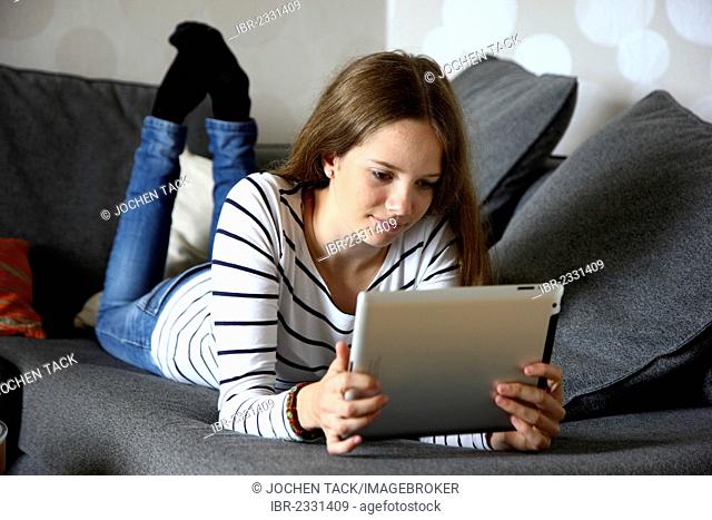 Girl lying on a sofa holding an iPad, tablet computer with wireless internet access