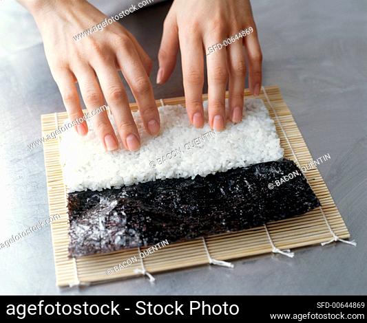 Making Maki Sushi: Hands Pressing Rice onto a Sheet of Nori