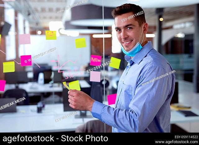 Portrait of caucasian businessman in lowered face mask brainstorming, smiling to camera