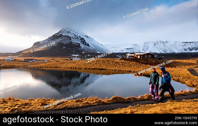 Arnarstap, Iceland - March 21 2016: People walking around a lake with snowy mountain reflected on the water at Arnarstapi area in Snaefellsnes peninsula in...