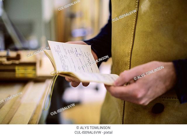 Close up of mid adult craftsman holding notebook in organ workshop